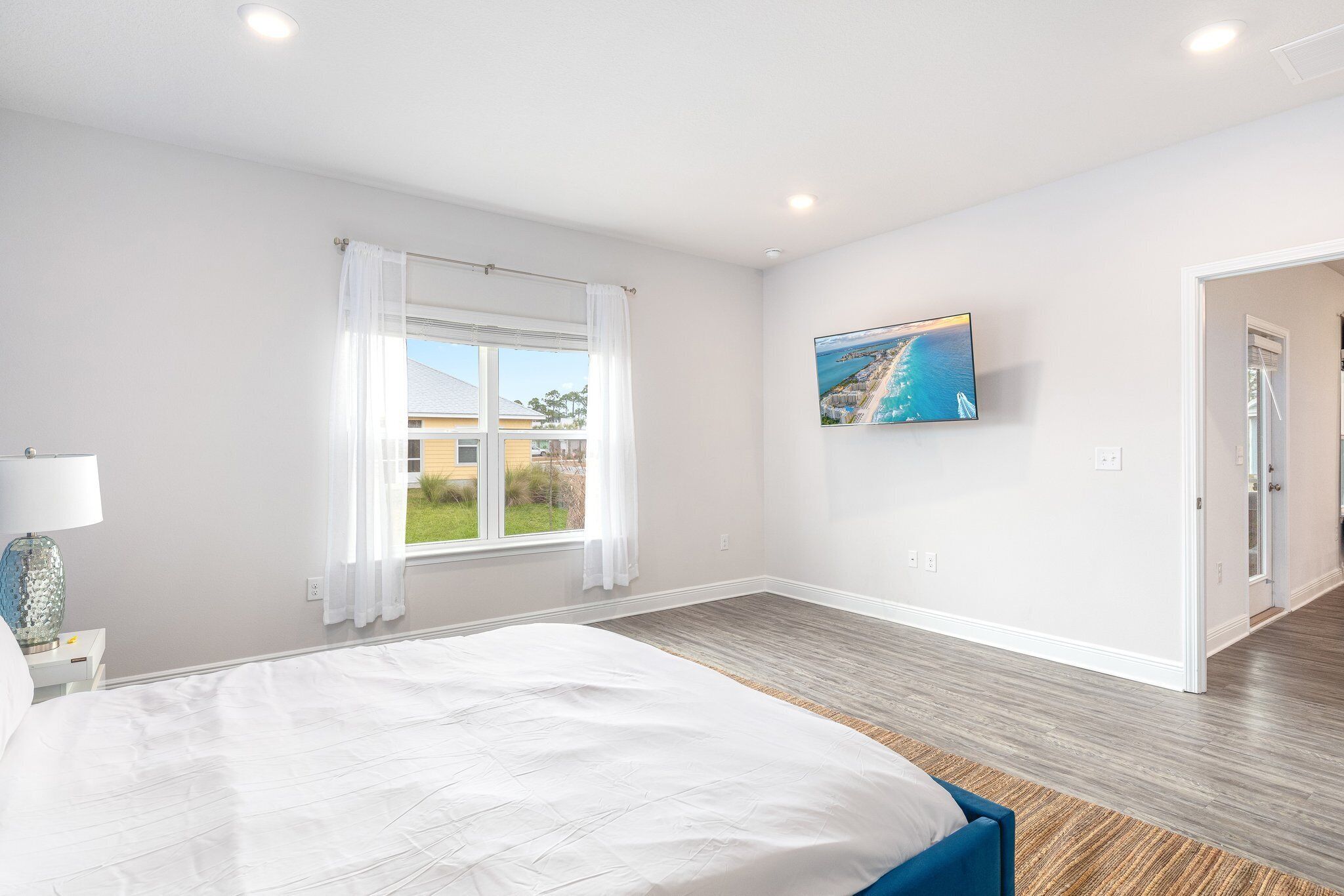 Un dormitorio con cama, televisor en la pared y ventana con cortinas.