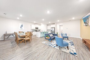 Un amplio salón con una mesa de comedor, sillones azules y una cocina al fondo.