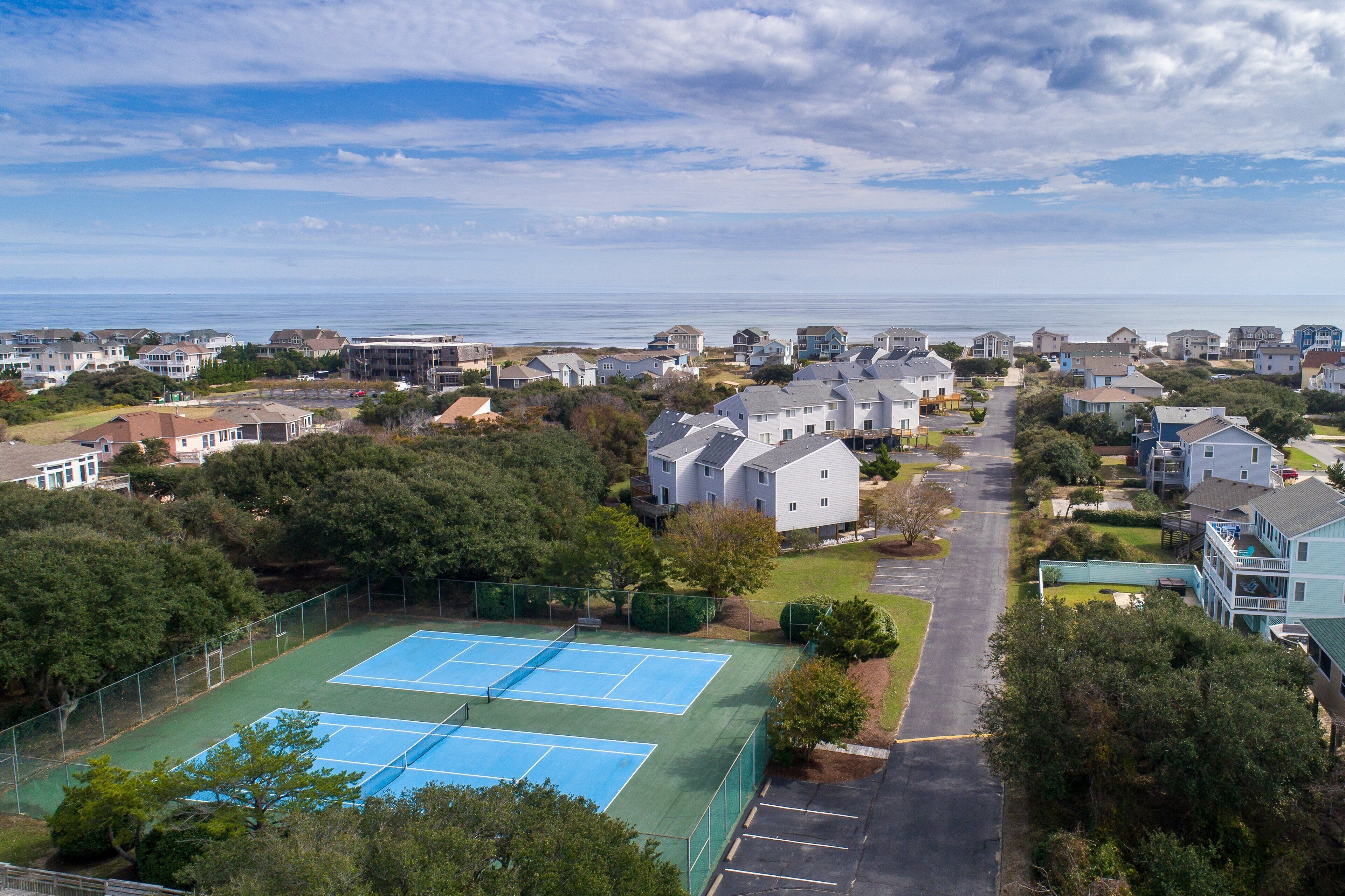 A residential area with houses, a tennis court, and a view of the ocean.