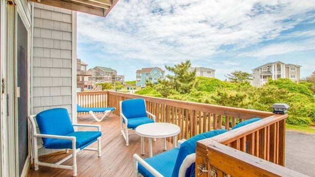 Terraza techada al aire libre con sillas azules y una mesa, con vista a una zona residencial.