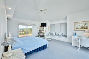 A bedroom with a large bed, a desk, a chair, a bookshelf, and a window with a view.