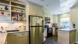A modern kitchen with a stainless steel refrigerator, microwave, and oven. There are wooden cabinets and a tiled backsplash. - 4601-Sandy Bluff - Southern Shores Home w/ Private Pool (Southern Shores)