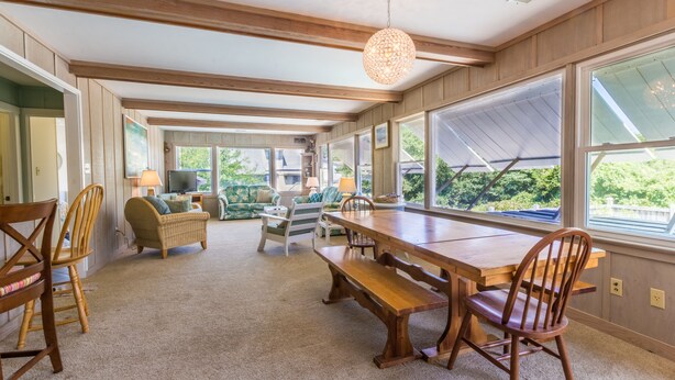 A spacious dining area with a wooden table and benches, surrounded by large windows offering views of greenery. - 4601-Sandy Bluff - Southern Shores Home w/ Private Pool (Southern Shores)
