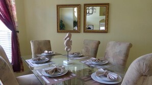 Un coin repas avec une table en verre dressée pour six personnes, entourée de chaises rembourrées. Deux miroirs encadrés sont accrochés au mur, au-dessus de la table.