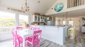 A bright kitchen with white cabinets, a pink dining table, and a large island. - 4751- Purple Passion - Walk to Beach | Pool, Hot Tub & Dogs Welcome (Kitty Hawk)