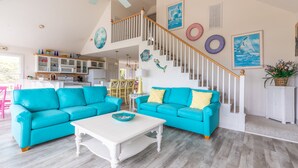 A spacious living room with two turquoise sofas, a white coffee table, and a staircase with a wooden railing. - 4751- Purple Passion - Walk to Beach | Pool, Hot Tub & Dogs Welcome (Kitty Hawk)