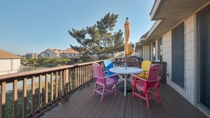 Une terrasse en bois avec une table et des chaises, un parasol jaune et une vue sur les maisons et les arbres des environs.