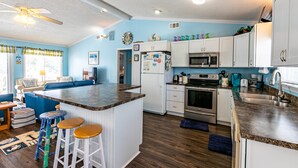 A modern kitchen with white cabinets, a central island with stools, a microwave, oven, and a refrigerator. - 5002 - Bohannon - Soundfront KDH Escape w/ Sunset Views (Kill Devil Hills)