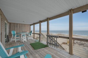 A wooden deck with a view of the beach, outdoor seating, and a small staircase leading to the beach.