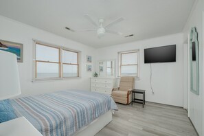 A bedroom with a bed, a chair, a dresser, a television, and a ceiling fan.