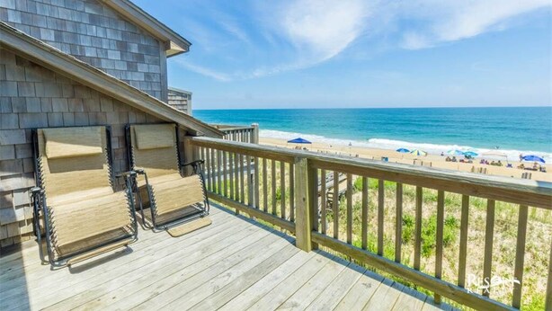 Een houten terras met twee ligstoelen met uitzicht op een strand met parasols.