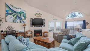 Een woonkamer met een televisie, bank, fauteuil, open haard en een groot raam.