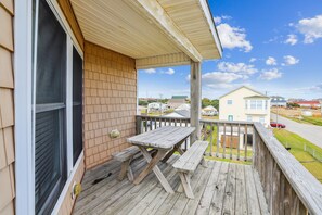 A wooden deck with a picnic table and benches, overlooking a residential area.