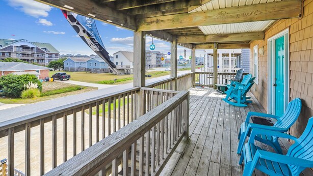 Een houten terras met blauwe stoelen, uitzicht op het strand en een gebouw met een blauwe deur.