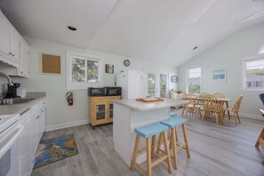 Een keuken met een centraal eiland, barkrukken, houten stoelen en een eettafel.
