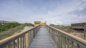 Une promenade en bois mène à une zone de plage où se trouve une structure en bois à l’extrémité.