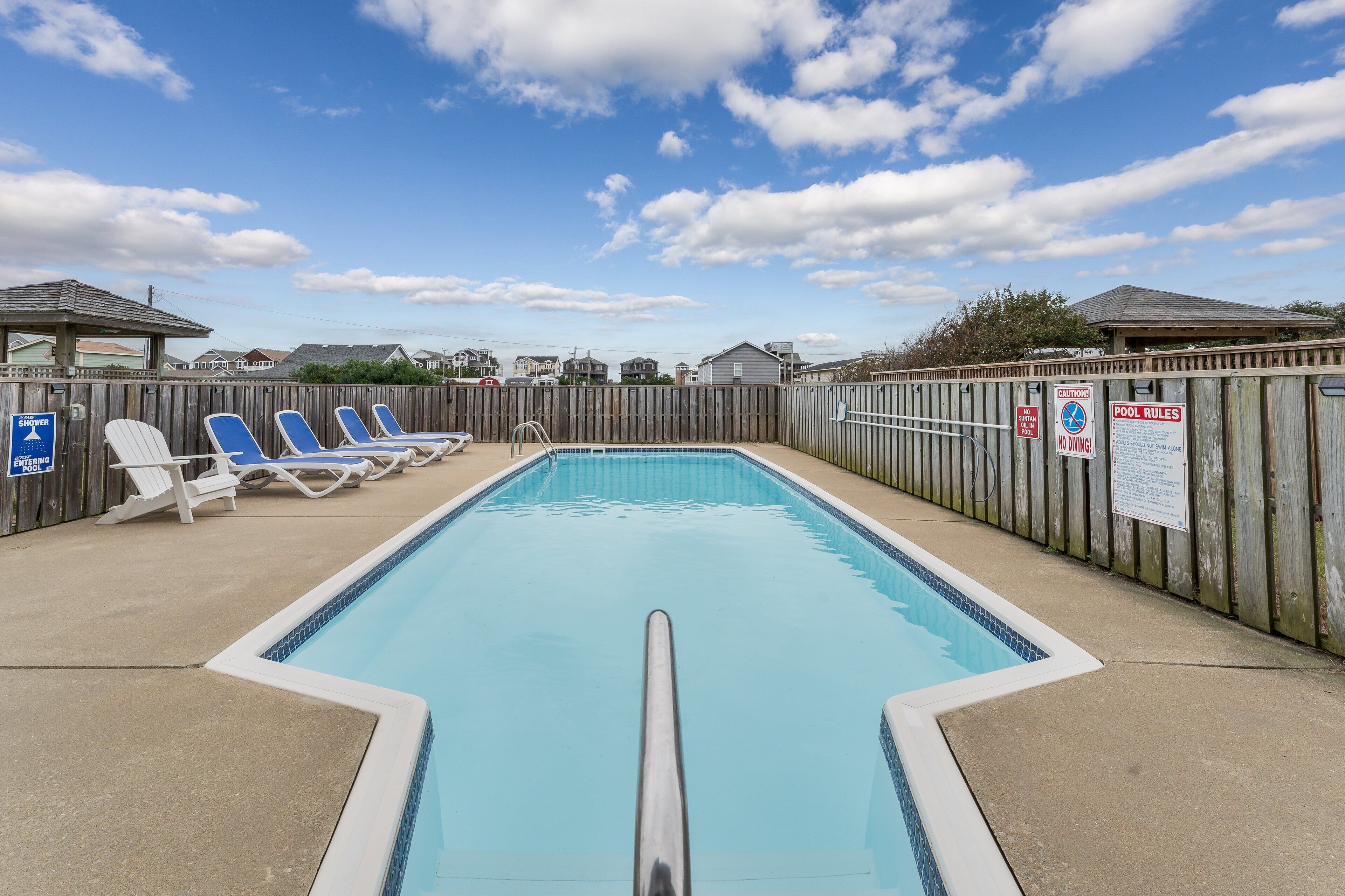 Une piscine entourée d’une cl ôture en bois, avec des chaises longues et un panneau indiquant qu’il est interdit de plonger.