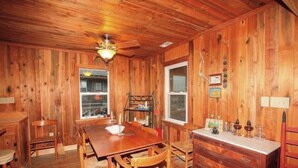 A wooden interior with a dining table, chairs, a chandelier, and a window. - 5443- Gillam Cottage, Oceanfront | Nags Head | Sleeps 8 (Nags Head)