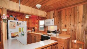 A compact kitchen with wooden walls, a refrigerator, a microwave, a stove, and a sink. - 5443- Gillam Cottage, Oceanfront | Nags Head | Sleeps 8 (Nags Head)
