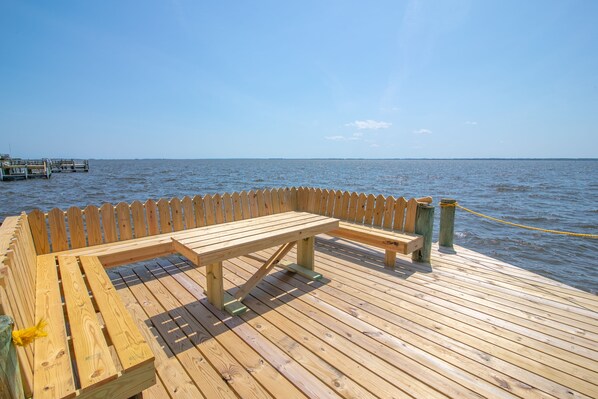 Une terrasse en bois, dotée de bancs et d’une barrière en corde, qui offre une vue sur une étendue d’eau.