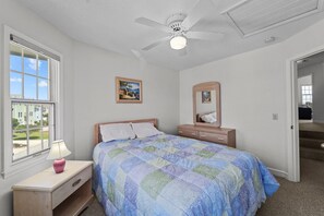 A bedroom with a bed, a nightstand, a dresser, a ceiling fan, a window, and a door leading to a staircase. - 5598-Serenity - Dog-Friendly Nags Head Duplex Retreat (Nags Head)