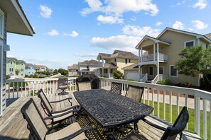 A wooden deck with a table and chairs, surrounded by a white fence, overlooking a residential area with houses. - 5598-Serenity - Dog-Friendly Nags Head Duplex Retreat (Nags Head)