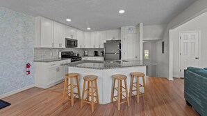 Eine moderne Küche mit weißen Schränken, einer Granitarbeitsplatte und einem Edelstahl-Kühlschrank. An der Kücheninsel stehen drei Holzstühle.