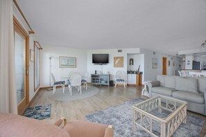Ein geräumiges Wohnzimmer mit einer Couch, Sesseln, einem Fernseher und einer Küchenzeile.
