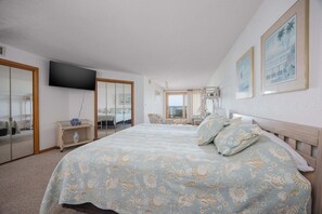 Quarto com uma cama grande, televisão na parede e vista para o exterior.