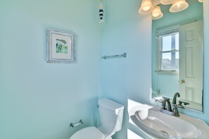 A bathroom with a toilet, sink, and a framed picture on the wall. - 5647- Sandy Pause - Nags Head Escape | Beach Club & Pool Access (Nags Head)