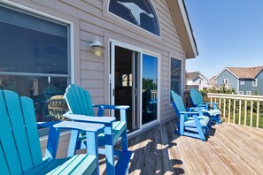 Een terras met blauwe Adirondack-stoelen en een glazen deur die leidt naar een overdekt gedeelte.
