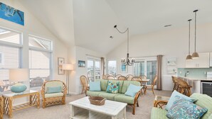 A spacious living area with a green sofa, wicker chairs, a white coffee table, and a dining table with chairs. - 5685- Seaside - Nags Head Coastal Home Near The Beach (Nags Head)