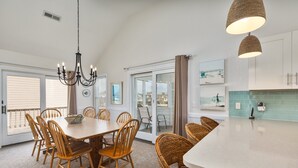 A dining area with a wooden table and chairs, a chandelier, and a view through a glass door to the outside. - 5685- Seaside - Nags Head Coastal Home Near The Beach (Nags Head)
