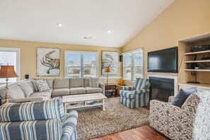 Relax in a cozy seating area with a sofa and armchairs, a flat-screen TV above a fireplace, and artwork on the walls.