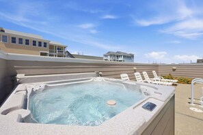 A hot tub with lounge chairs, a clear sky, and a building in the background. - 5702- It's A Wonderful Life, Steps to Beach | Pool, Hot Tub & Game Room (Nags Head)