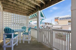 A covered outdoor area with a wooden deck, white lattice fence, and a view of buildings in the background. - 5702- It's A Wonderful Life, Steps to Beach | Pool, Hot Tub & Game Room (Nags Head)