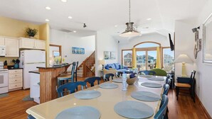 A spacious kitchen with white cabinets, a wooden island, and a dining area with blue chairs and a large table. - 5702- It's A Wonderful Life, Steps to Beach | Pool, Hot Tub & Game Room (Nags Head)