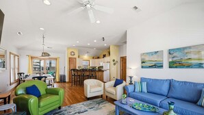 A spacious living area with a sofa, chairs, a coffee table, and a kitchen in the background. - 5702- It's A Wonderful Life, Steps to Beach | Pool, Hot Tub & Game Room (Nags Head)