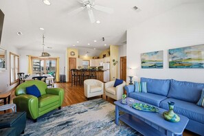 A spacious living area with a sofa, chairs, a coffee table, and a kitchen in the background.