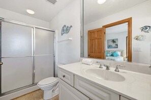 Ein Badezimmer mit einem weißen Waschbecken, zwei Wasserhähnen, einem Spiegel, einer Toilette und einer matten Duschkabine.