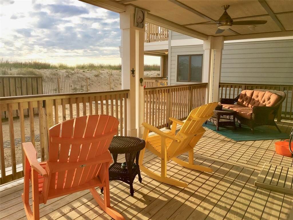 A covered deck with a view of the beach, featuring two rocking chairs and a small table.