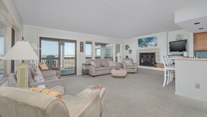 A spacious living area with a large window, a fireplace, and a kitchen area.