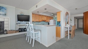 A compact kitchen with a central island, a dining area with a white table and chairs, and a television on a stand.