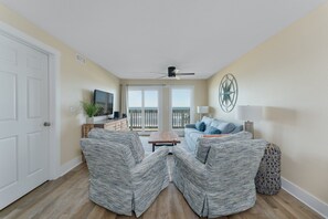 Un salon comprenant deux fauteuils rembourrés, une table basse, un canapé, un téléviseur et un élément décoratif mural.