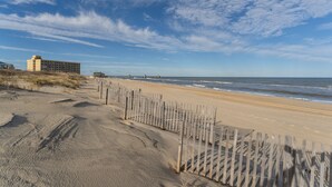 Une plage bordée d’une clôture en bois, un hôtel en arrière-plan et une jetée qui s’avance dans l’eau.