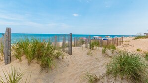 A sandy beach with a wooden fence and beach umbrellas. - 5782-Whale of a View - Charming Oceanfront Nags Head Cottage (Nags Head)