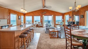 A spacious kitchen with a large island, wooden cabinets, and a view of the ocean. - 5782-Whale of a View - Charming Oceanfront Nags Head Cottage (Nags Head)