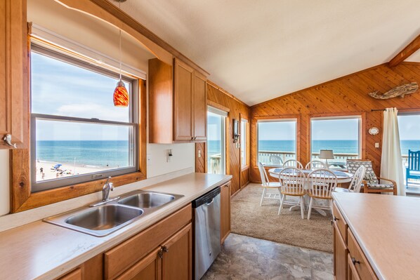 Enjoy a beachside meal in this kitchen with a view, featuring a stainless steel sink and dishwasher, wooden cabinets, and a countertop.