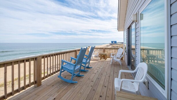 A wooden deck with rocking chairs and a table overlooking the ocean. - 5782-Whale of a View - Charming Oceanfront Nags Head Cottage (Nags Head)
