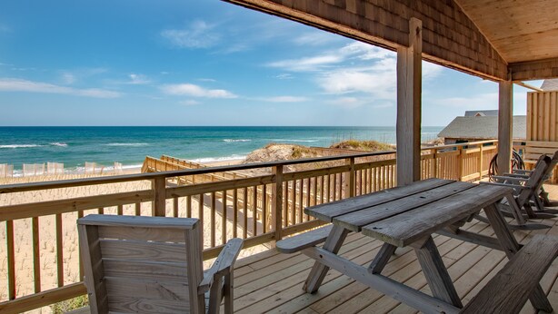 Una terraza de madera con mesas y sillas de picnic con vista a la playa.